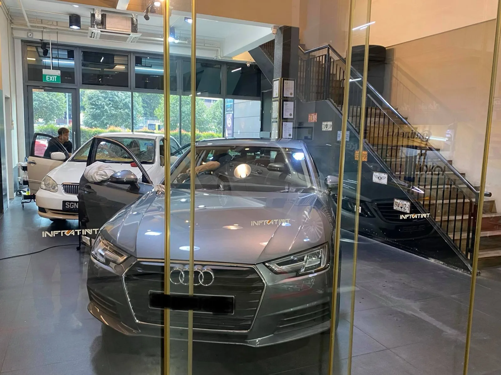 Grey Audi A4 sedan viewed through glass at Infratint Singapore window tinting bay