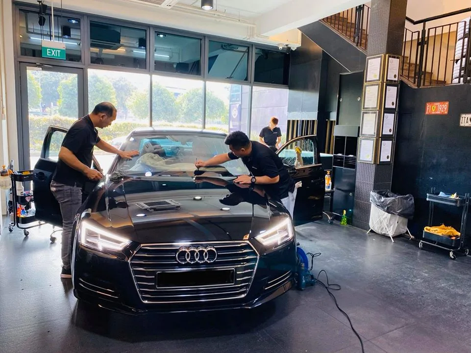 Black Audi A4 sedan having window film installed by two technicians at Infratint Singapore