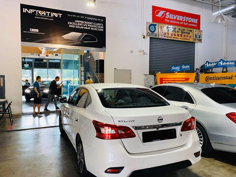 White Nissan Sylphy sedan beside a Mercedes-Benz under the Infratint banner at Infratint Singapore