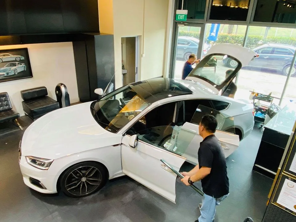 Technician squeegeeing the door glass of a white Audi A5 during window tinting at Infratint Singapore