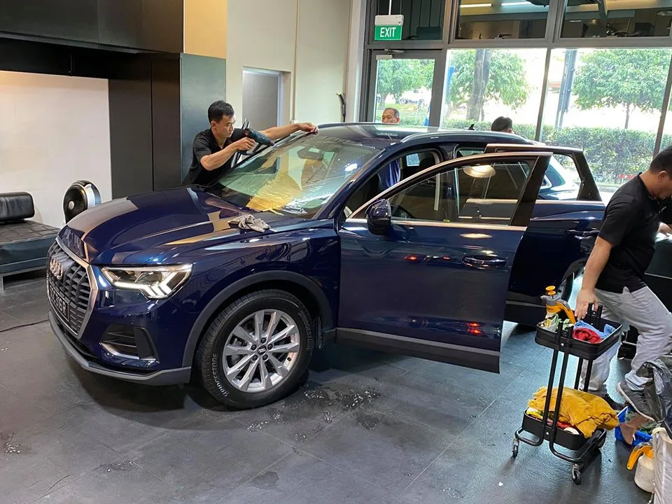 Installer applying window film to the windscreen of a blue Audi SUV at Infratint Singapore