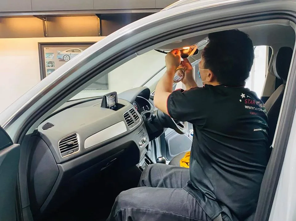 Technician applying window film to an Audi Q3 windscreen interior at Infratint Singapore