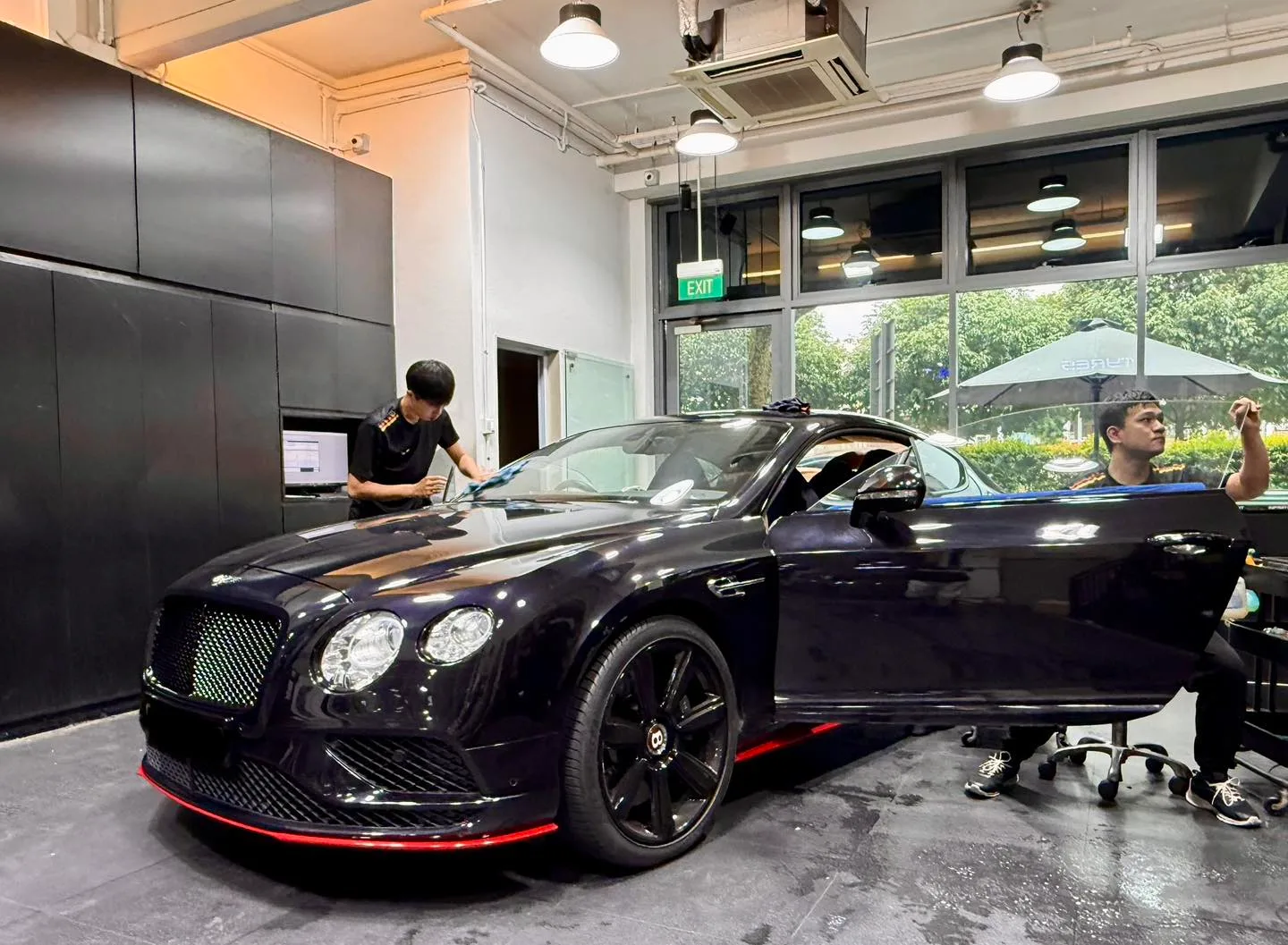 Two technicians tinting a black Bentley GT inside Infratint Singapore workshop