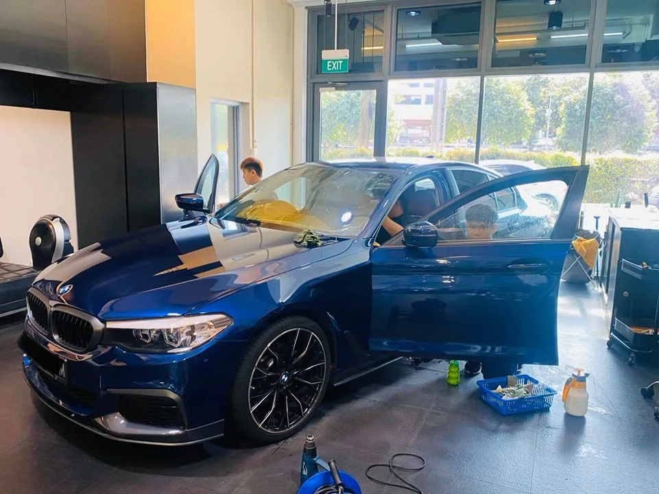 Blue BMW 5 Series front three-quarter with installers fitting tint at Infratint Singapore