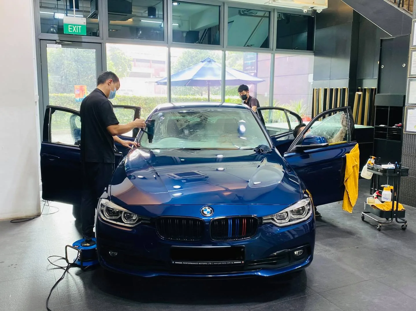 Technician tinting the windscreen of a blue BMW 3 Series at Infratint Singapore