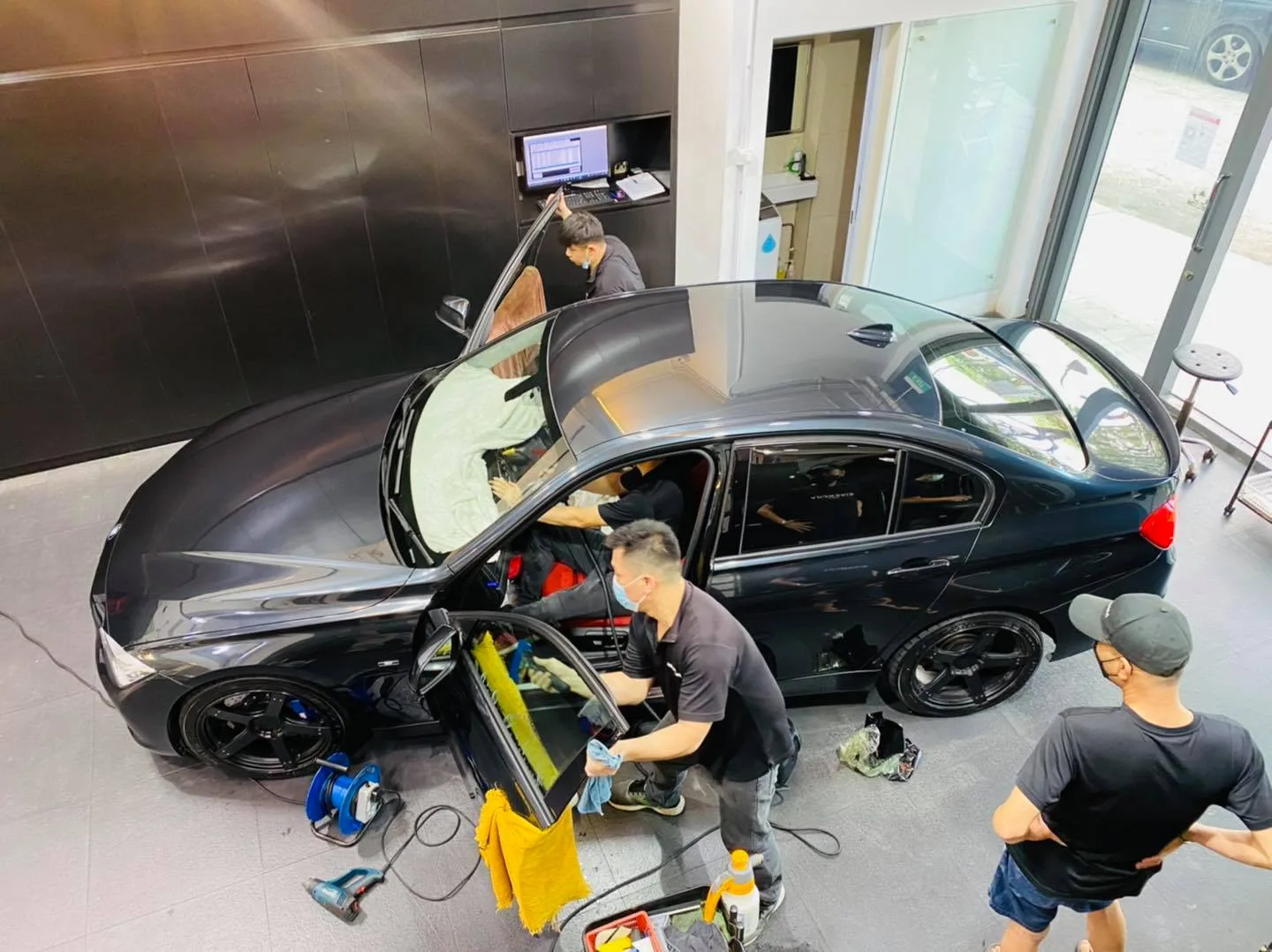 Overhead view of three installers tinting a black BMW sedan at Infratint Singapore