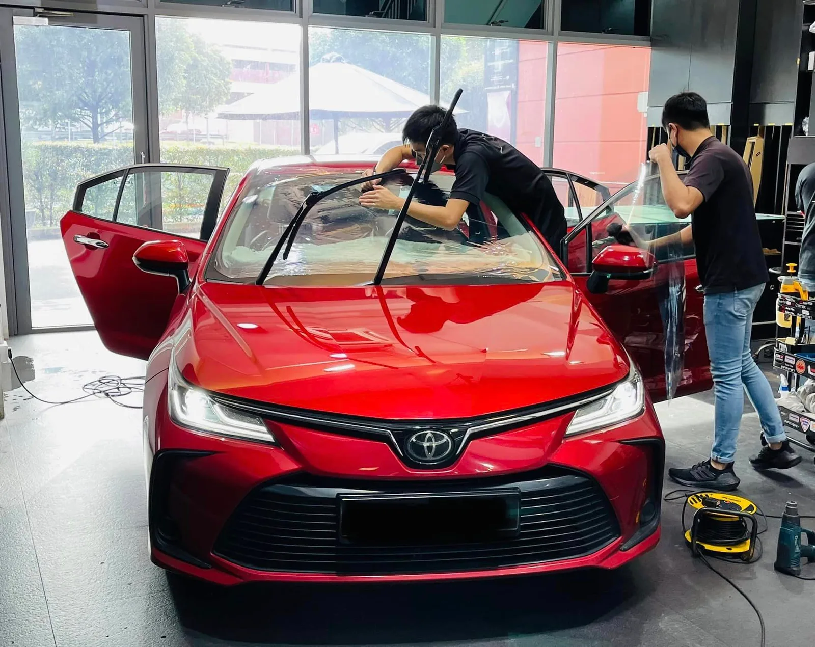 Red Toyota sedan being tinted by two technicians at Infratint Singapore