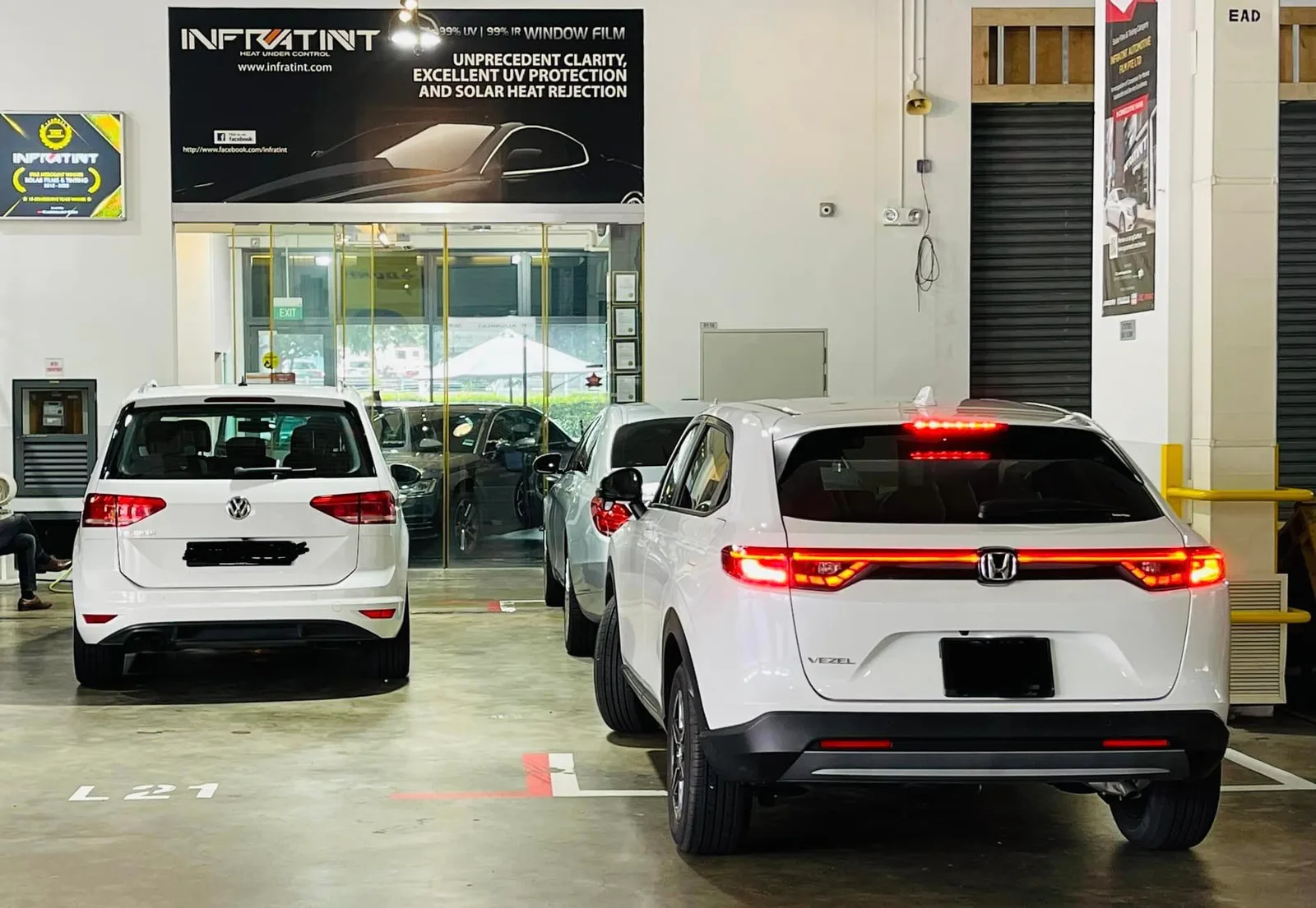 White Volkswagen Touran and white Honda Vezel parked under the Infratint Singapore banner
