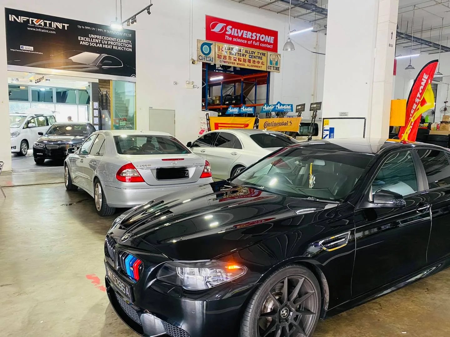 Black BMW M5 sedan in the install bay with a silver Mercedes-Benz E-Class at Infratint Singapore