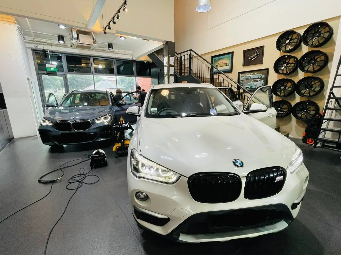 White BMW X1 SUV and a dark BMW inside Infratint Singapore beside a wheel display