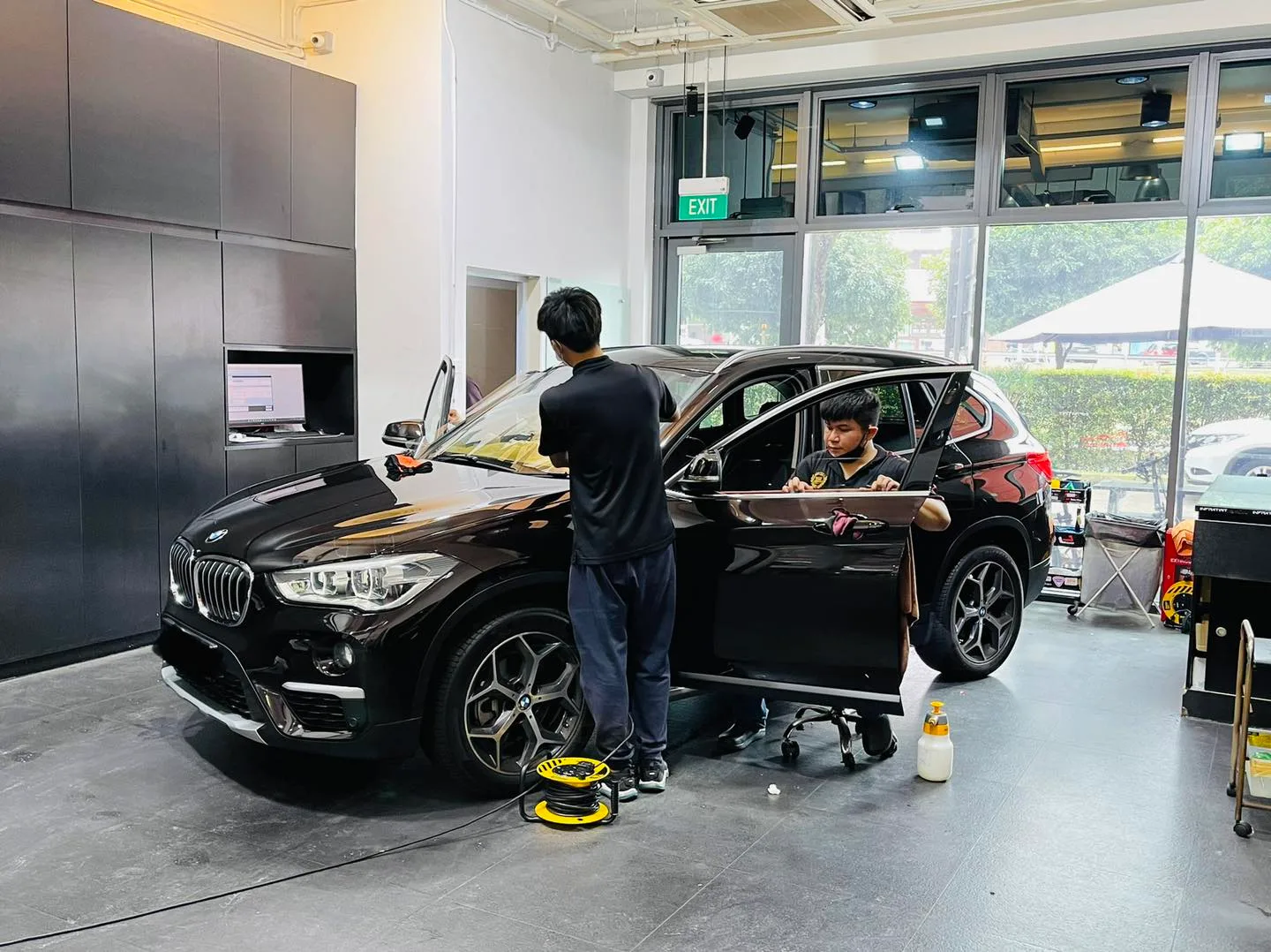 Two technicians tinting a dark BMW X1 with doors open at Infratint Singapore