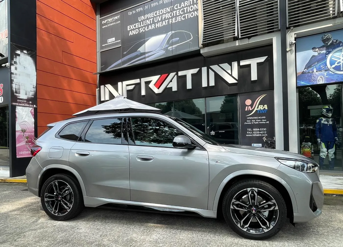 Tinted silver BMW X1 side profile outside the Infratint shopfront in Singapore
