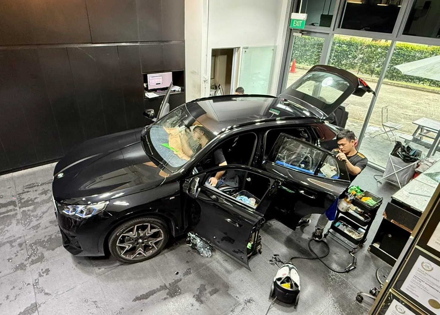 Installer applying tint film to a black BMW X2 rear door inside the Infratint workshop