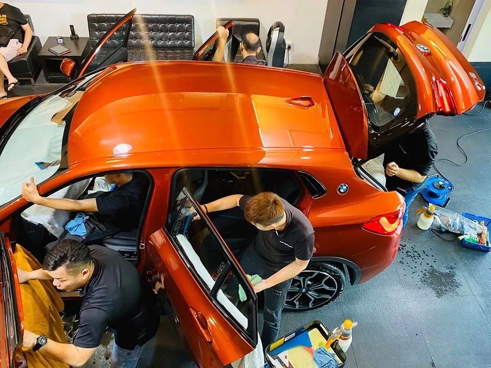 Team applying window tint to an orange BMW X2 with all doors open at Infratint Singapore
