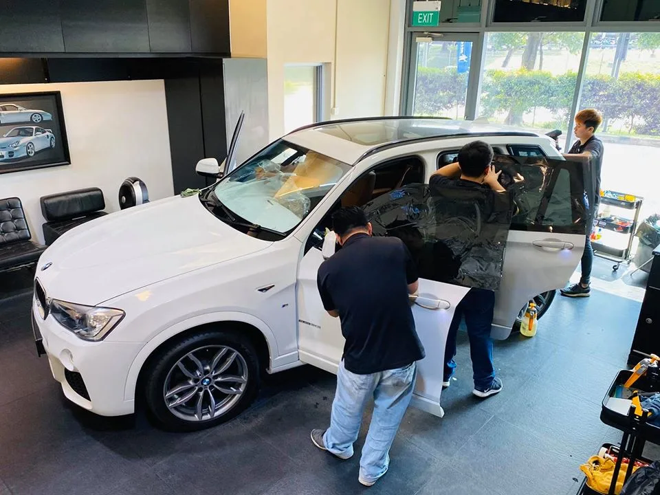 Technicians fitting tint film to the rear window of a white BMW X3 at Infratint Singapore