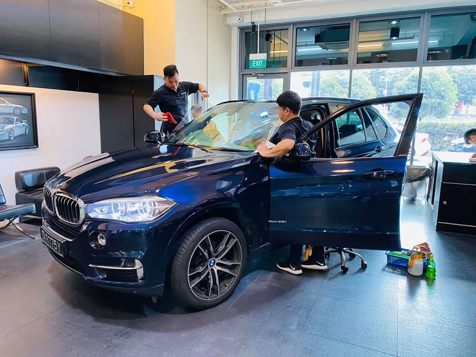 Technicians applying window film to a dark blue BMW X5 at Infratint Singapore