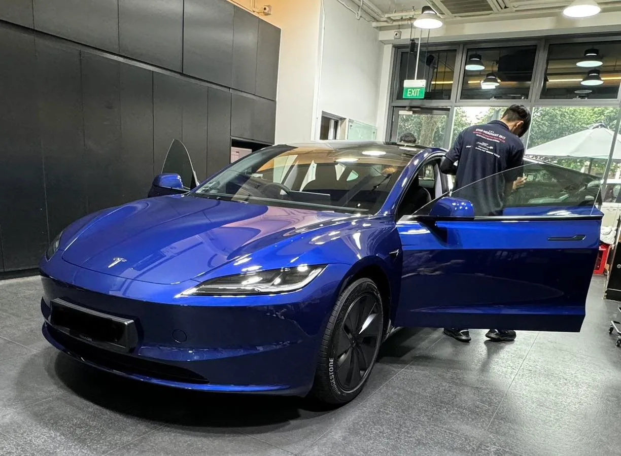 Blue Tesla M3H front three-quarter inside Infratint Singapore workshop during door glass install