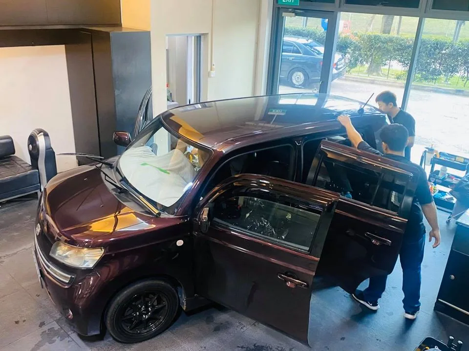 Technicians tinting the side windows of a maroon Daihatsu Materia at Infratint Singapore