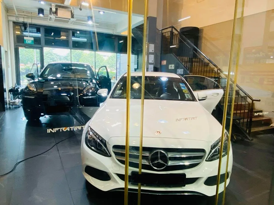 White Mercedes-Benz sedan and black Porsche Cayenne inside the Infratint Singapore showroom
