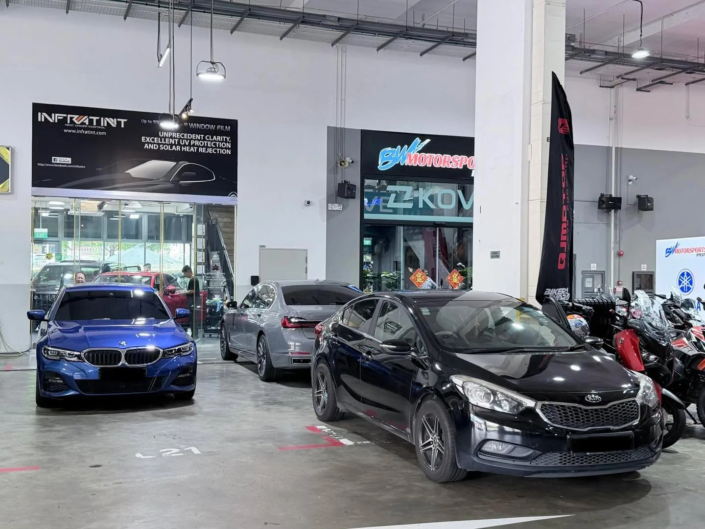 A blue BMW, a silver sedan, a black Kia, and a red motorcycle in an open workshop space.