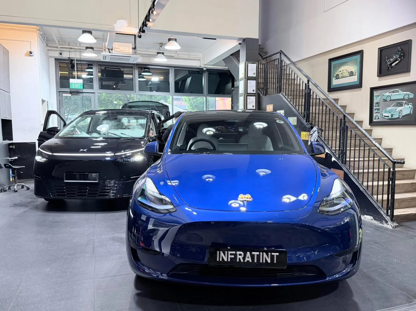 A blue Tesla Model Y parked indoors with the INFRATINT nameplate visible on the bonnet.