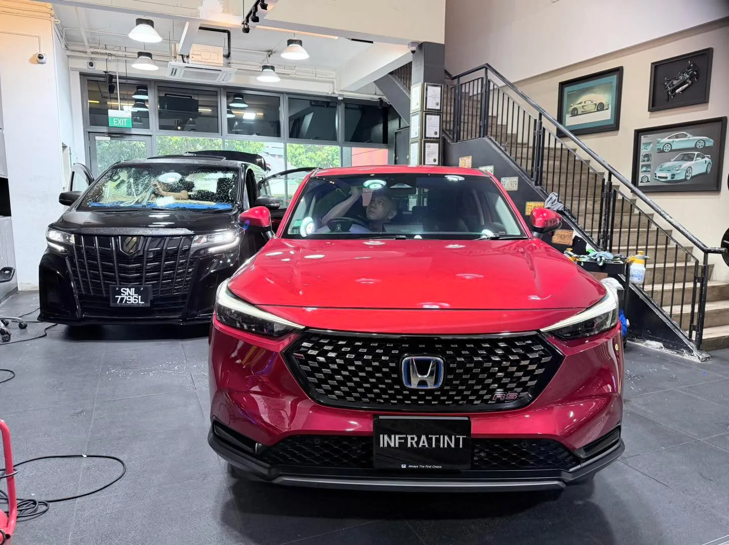 A red Honda Vezel and a black car with visible grille in the workshop.
