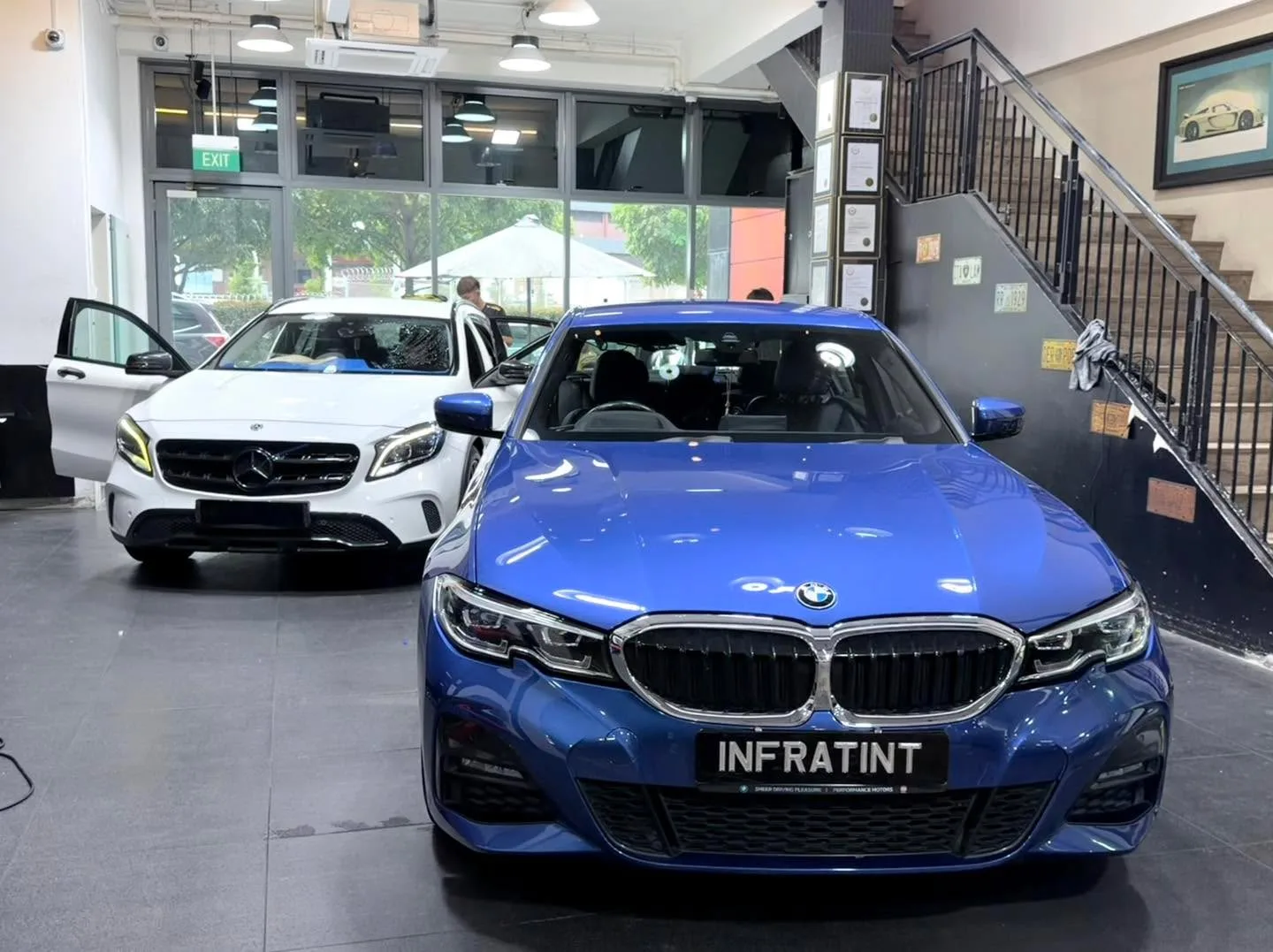 A blue BMW 330 sedan and a white Mercedes-Benz GLA 180 in the workshop.