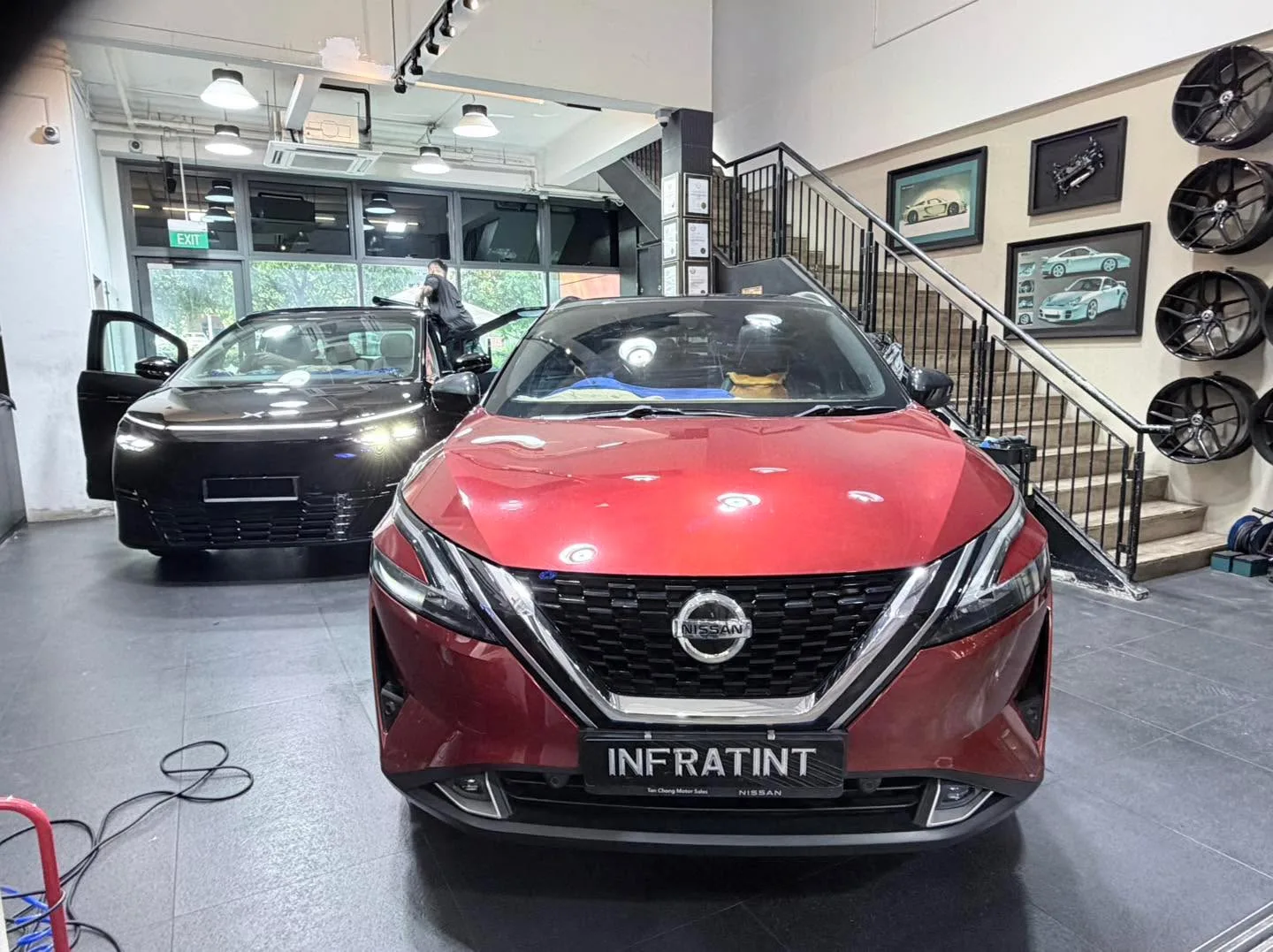 A red Nissan Qashqai and a black car with doors open in the workshop.