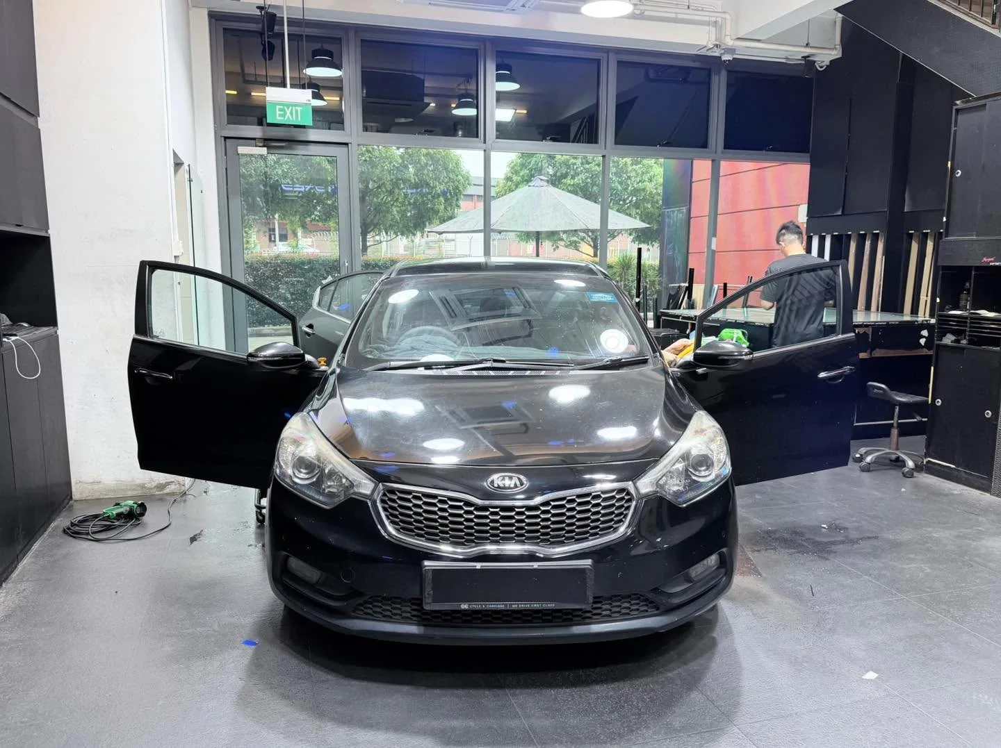 A black Kia Cerato with both doors open, parked indoors.