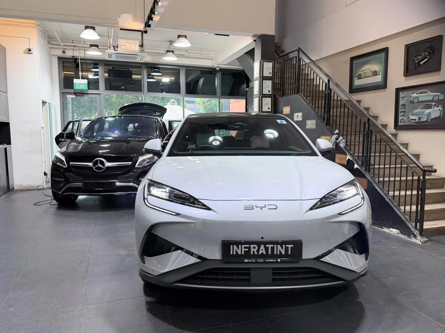 White Tesla sedan with blue BYD Atto 3 behind it indoors.
