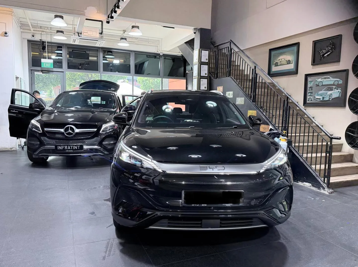 Black BYD Sealing 7 SUV and white Tesla sedan indoors.