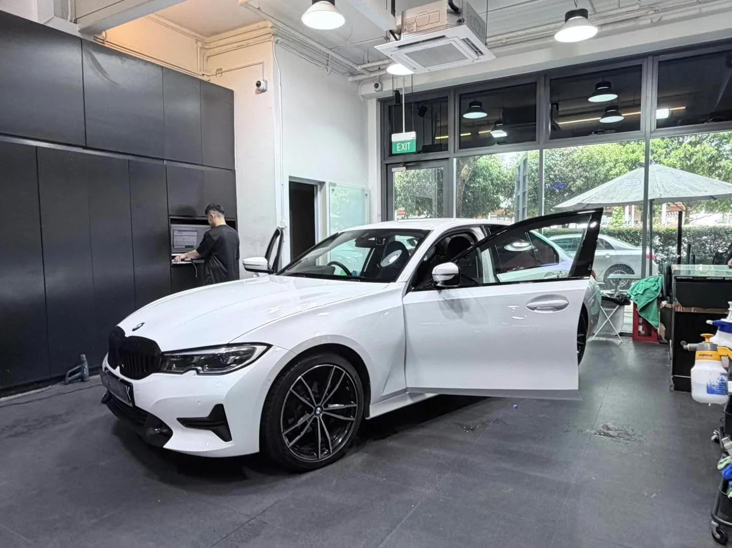 White BMW 3 Series with open door during tinting work indoors.