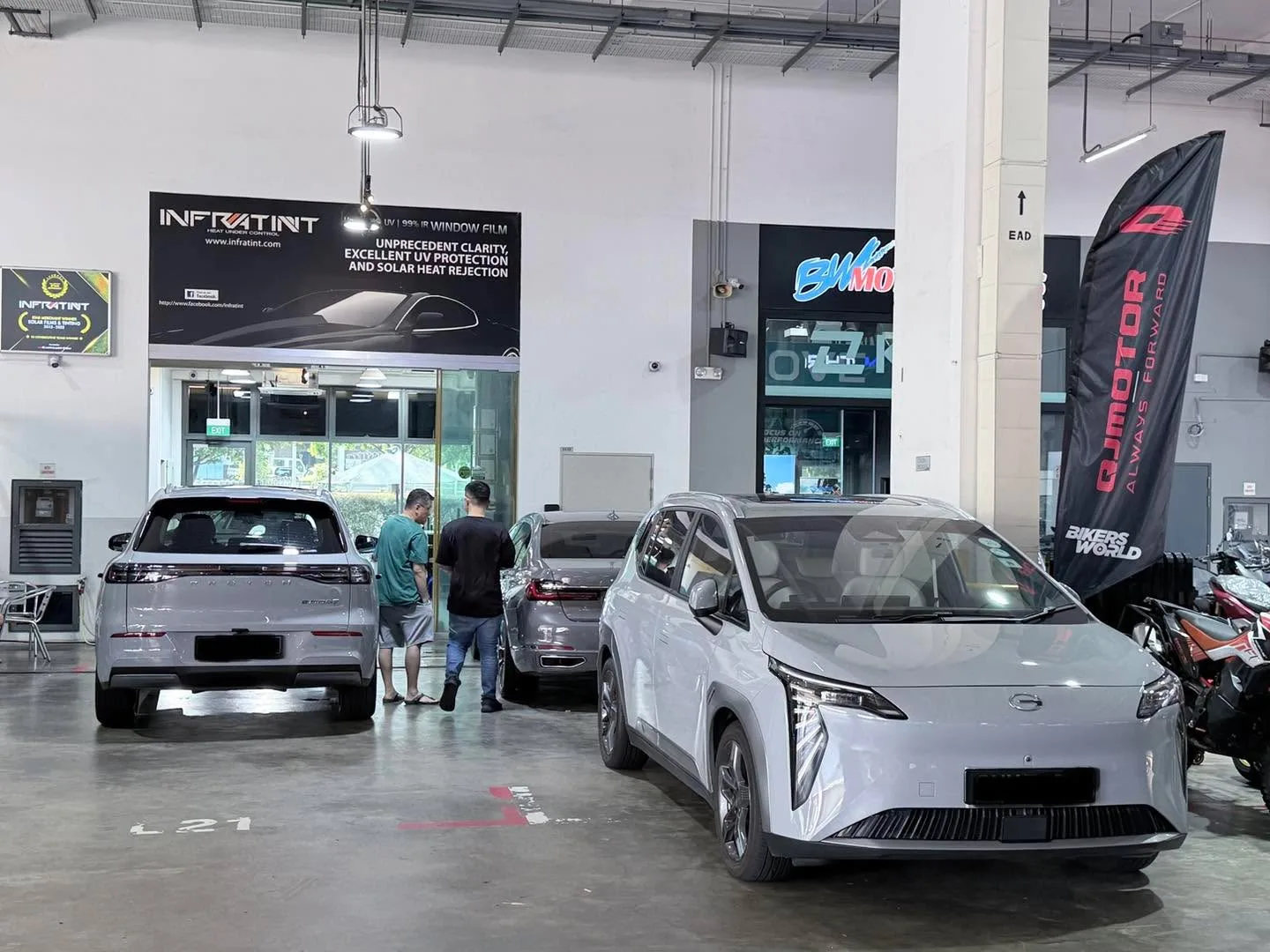 A white electric saloon and a silver SUV parked in the Infratint workshop with technicians working alongside.