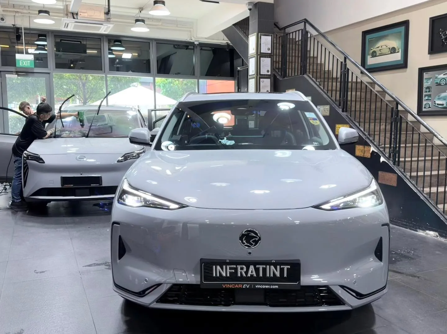 A white electric saloon with distinctive front grille, viewed from the front in the workshop.