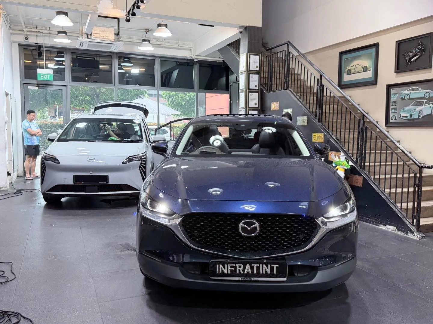A black SUV and a white electric saloon parked side by side in the workshop.