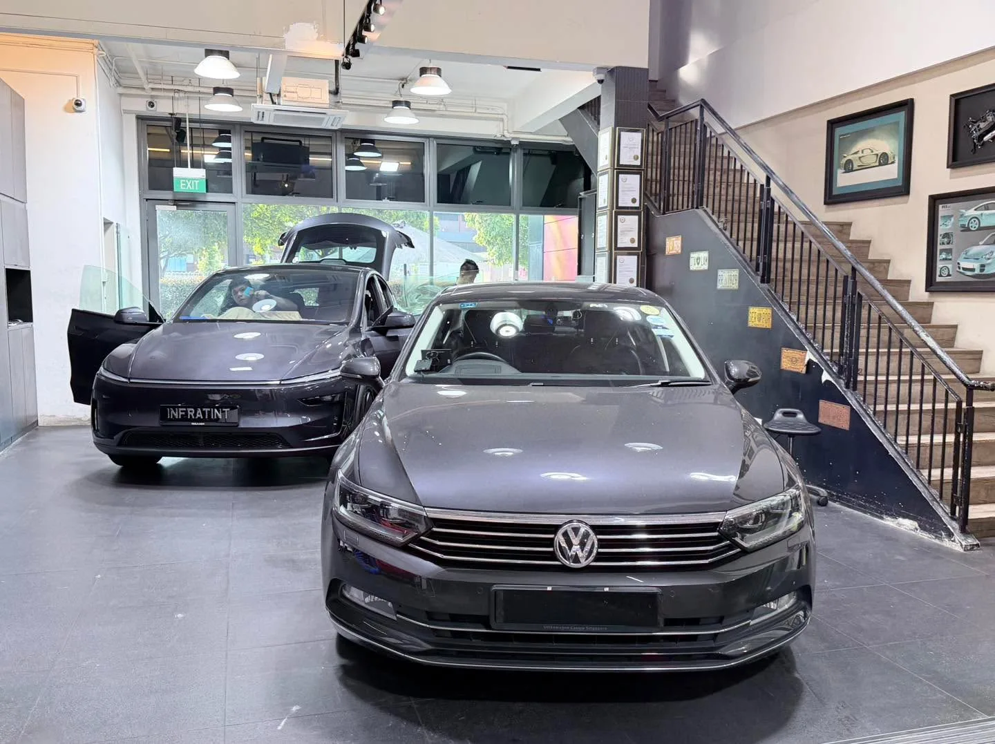 A dark-coloured sedan and a white electric saloon with open doors in the workshop.