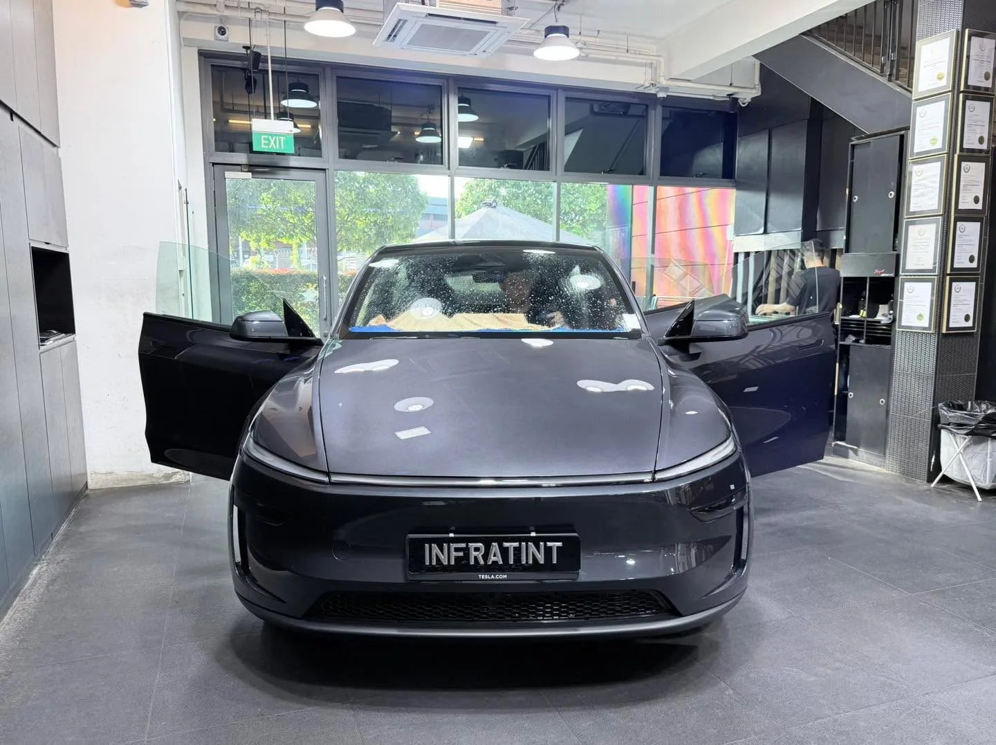 A dark blue electric saloon with falcon-wing doors open in the workshop.