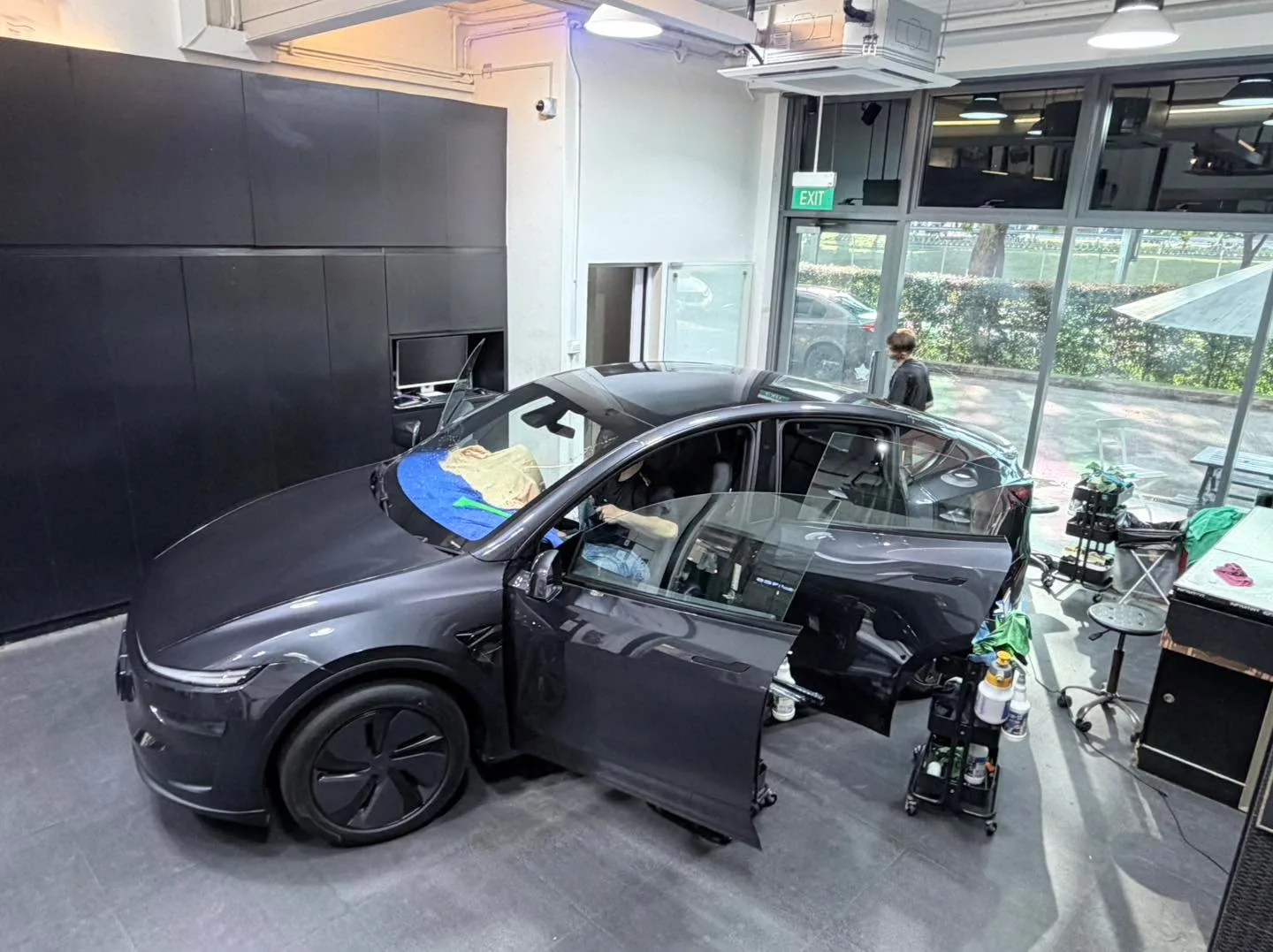 A red compact hatchback with all four doors and boot open, workers tinting windows inside the workshop.