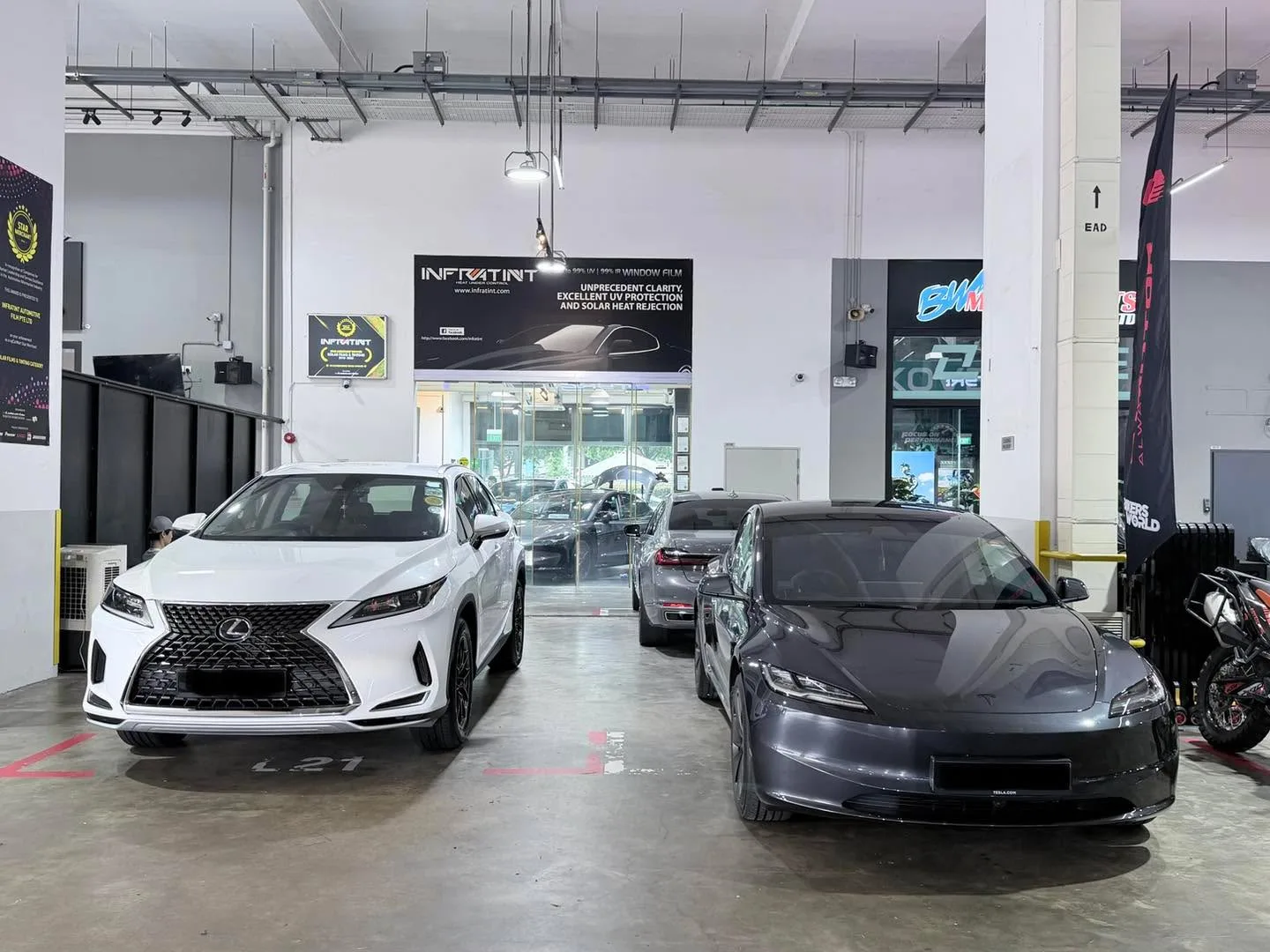 A white Lexus RX300 and dark grey Tesla Model 3 parked side by side inside the workshop.