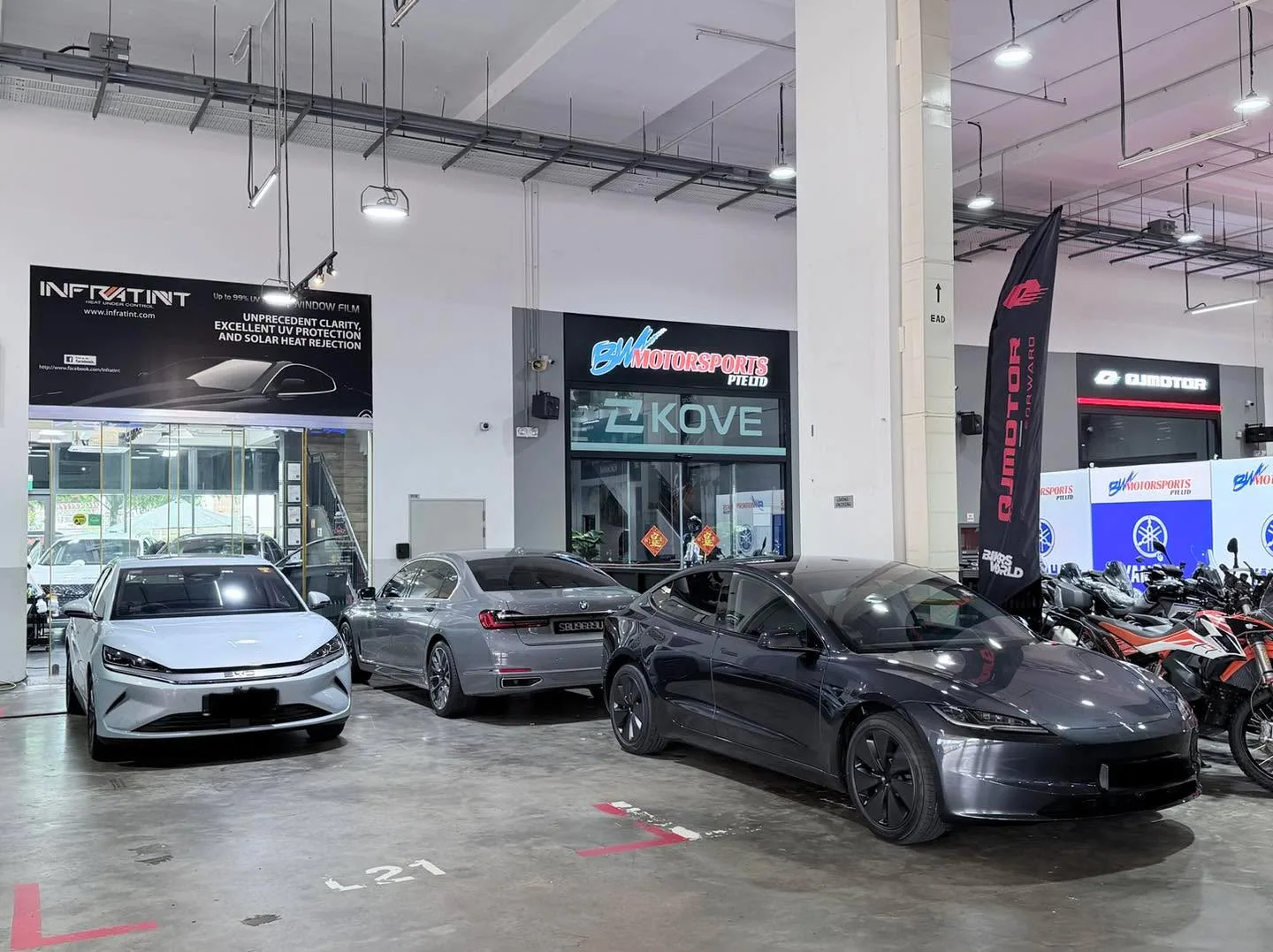 A white Tesla Model Y, a grey BMW sedan and a dark grey Tesla sedan parked in the workshop.