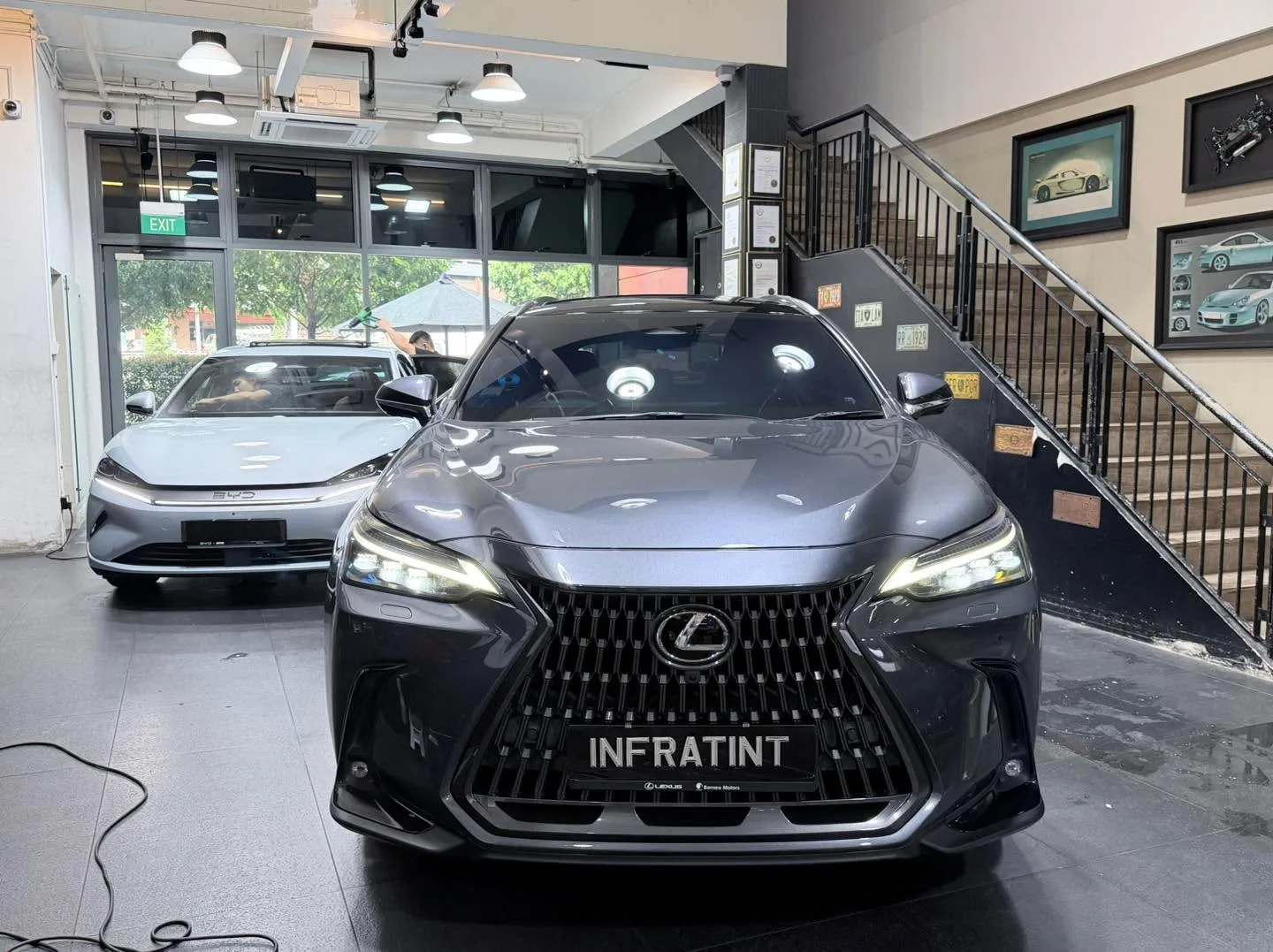 A black Lexus with distinctive mesh grille and white Tesla sedan facing the camera.