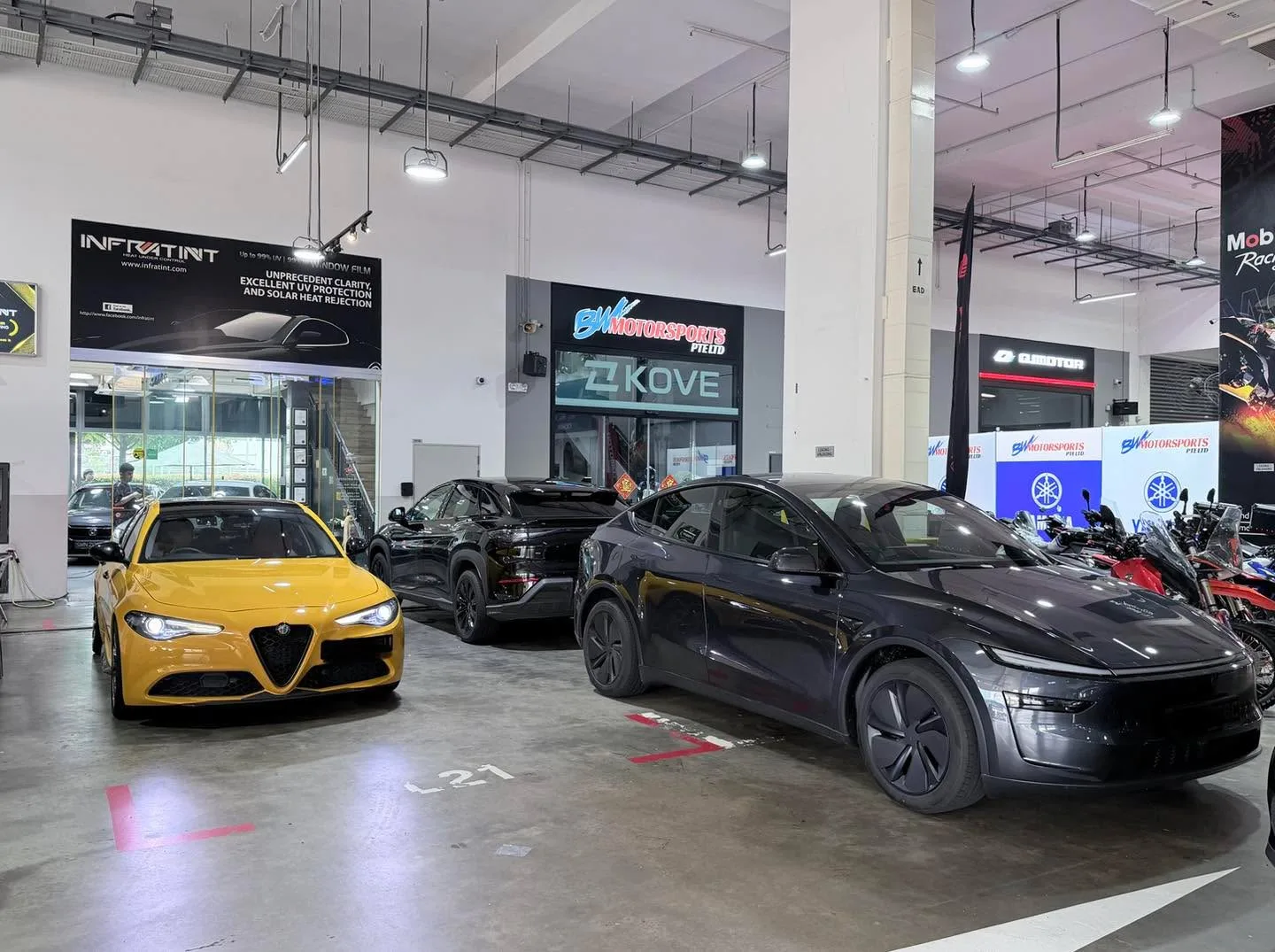 A yellow sports saloon, two black coupes and a red motorcycle inside a workshop space.