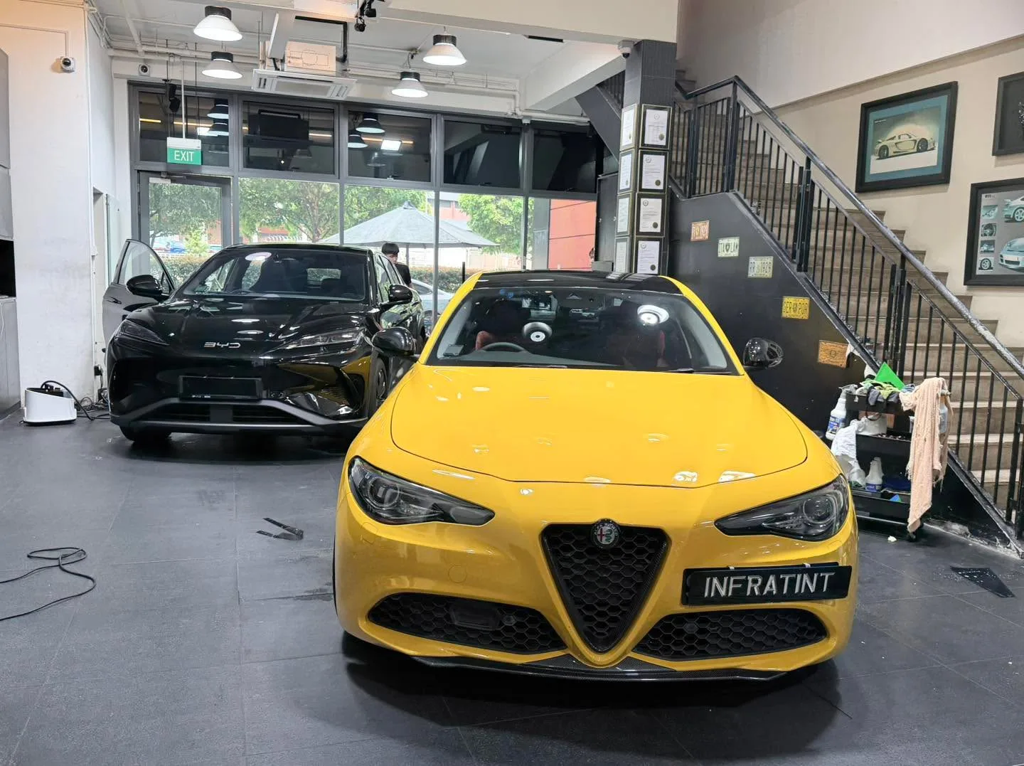 A yellow sports saloon and a black electric saloon with open doors in a workshop garage.