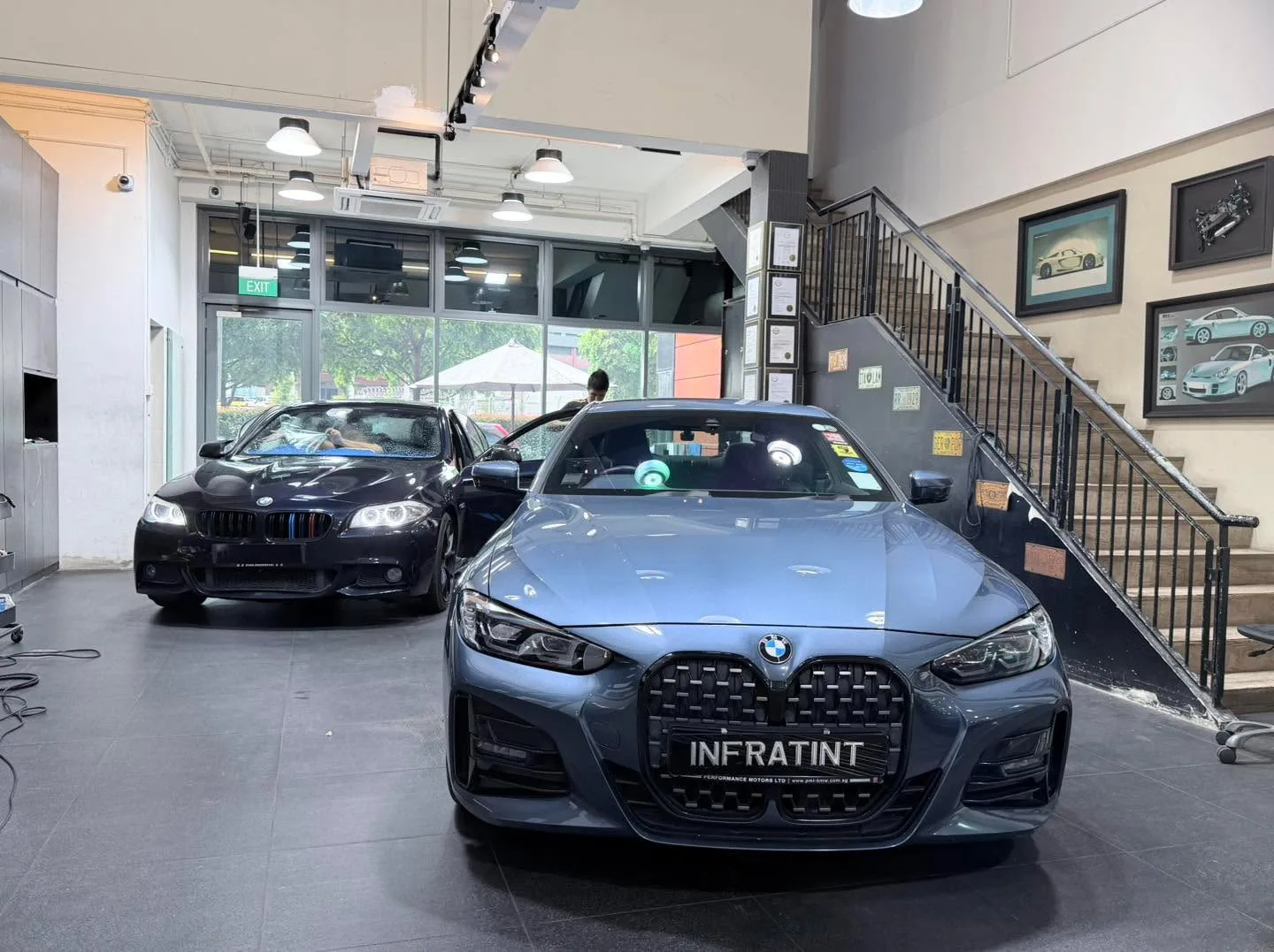 Two grey-blue BMW saloons, one in the foreground, inside a workshop space.