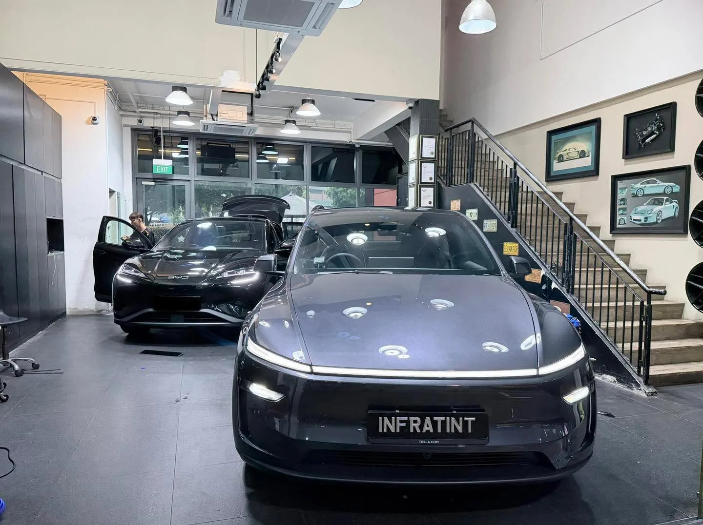 A dark grey or black electric saloon and a black saloon in a workshop interior.