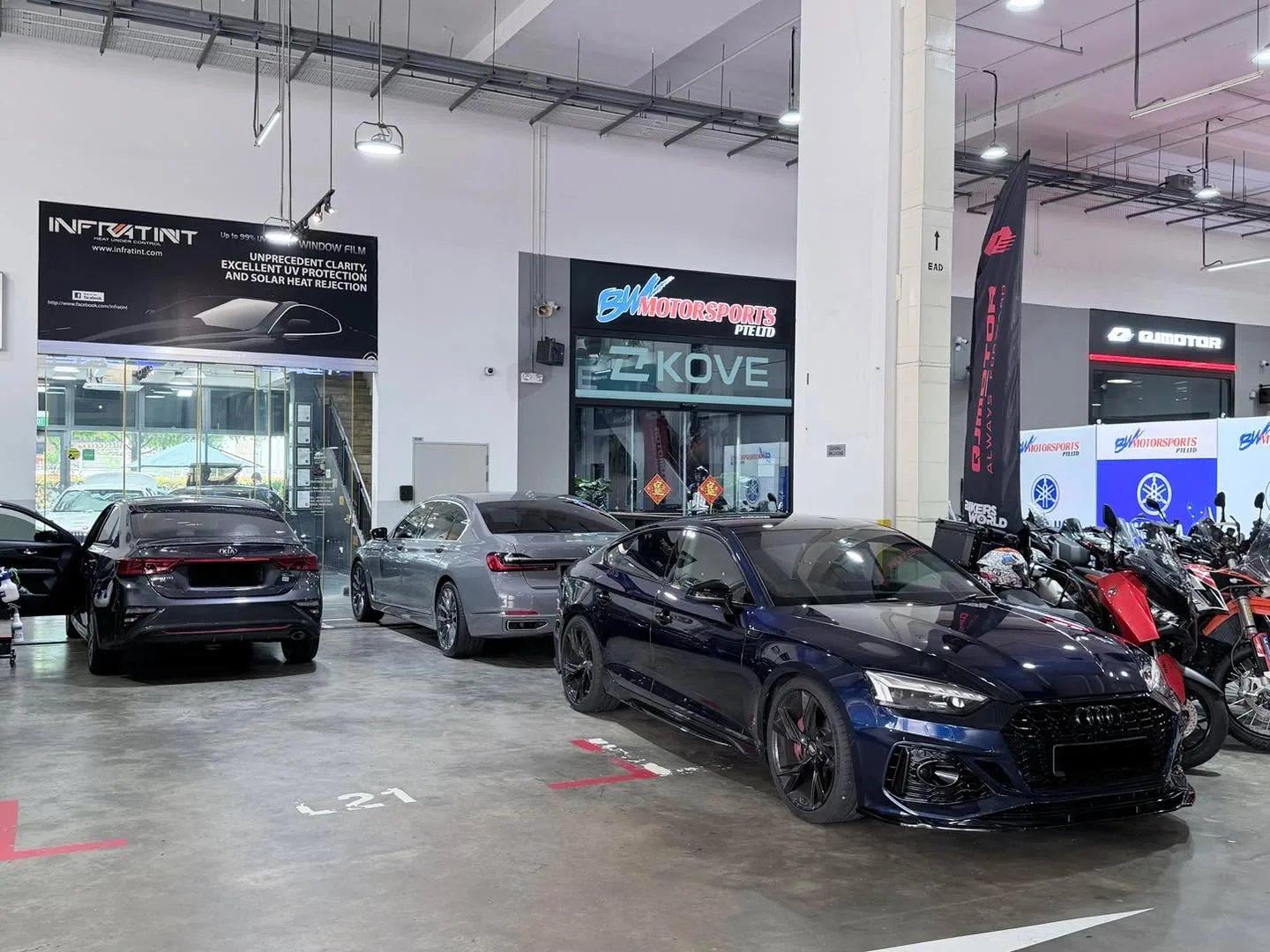 A dark blue Audi sedan and a dark red sedan at the Infratint workshop floor with Infratint signage visible.