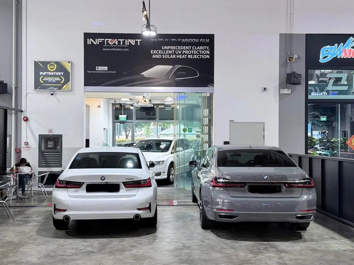 A white BMW 3 Series sedan and a silver BMW sedan parked in front of the Infratint storefront.
