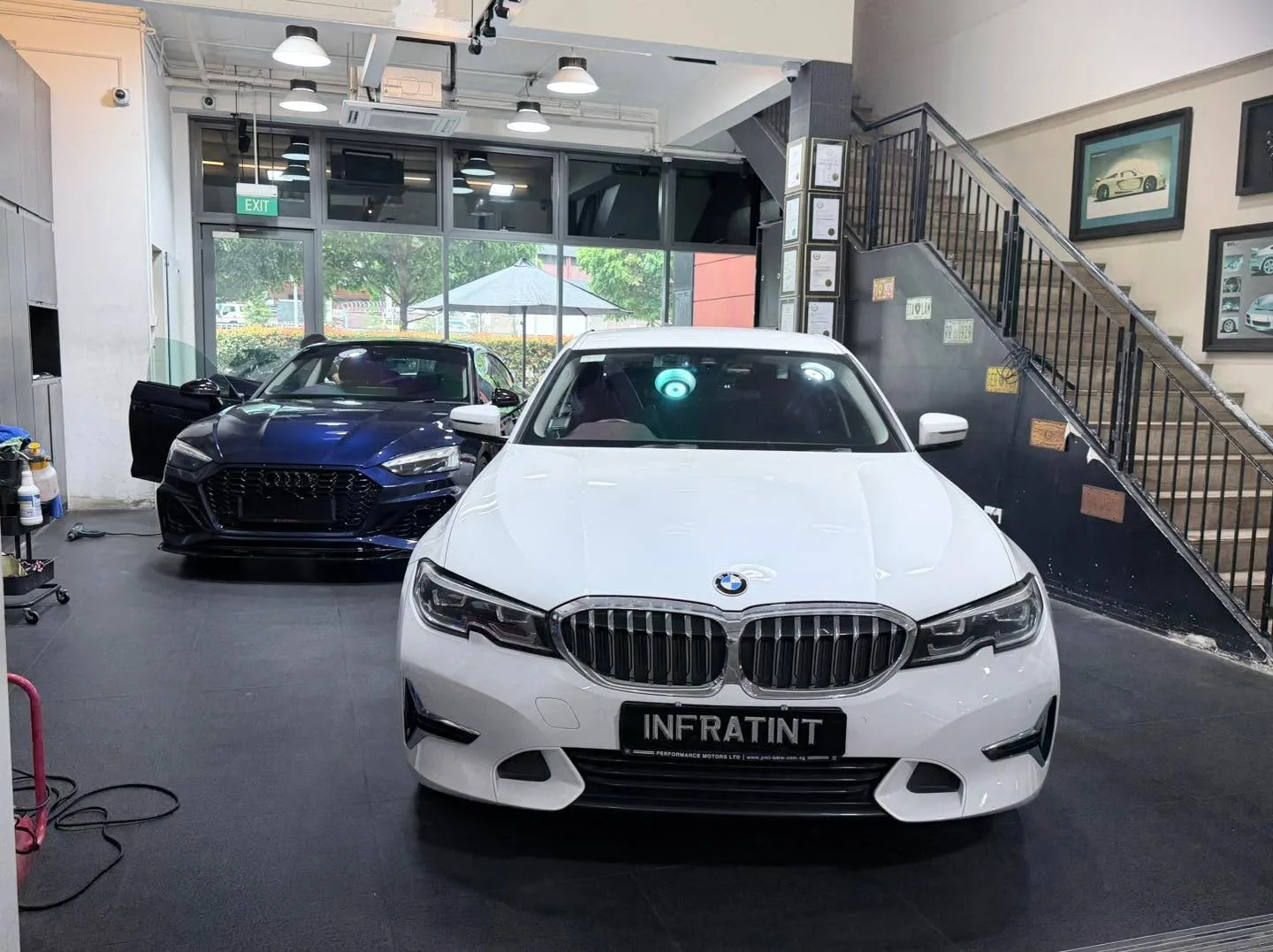 A white BMW 3 Series sedan positioned in the centre of the workshop floor with another blue car visible behind.