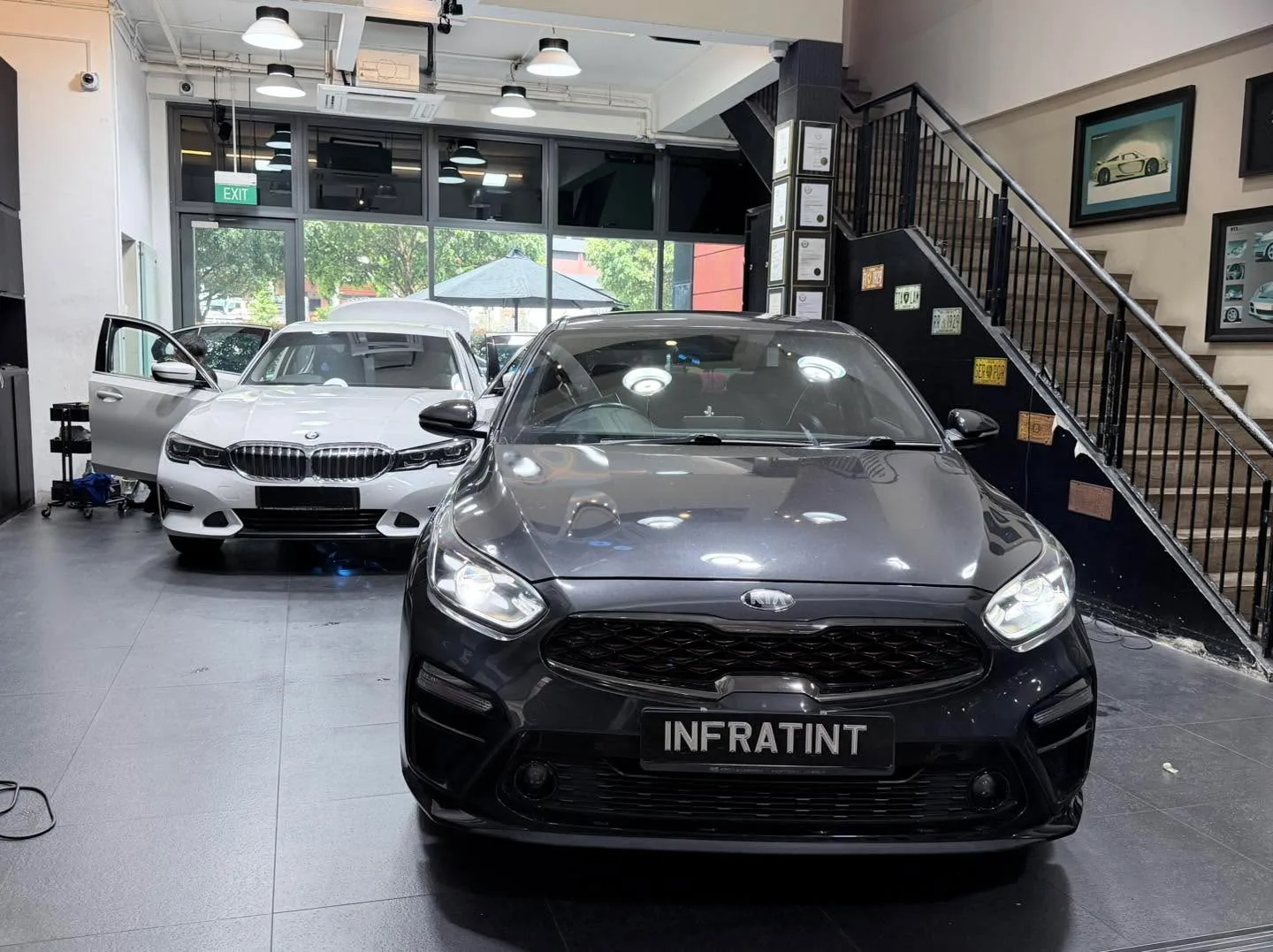 A white BMW 3 Series sedan and a black car visible at the Infratint workshop with large windows and signage.