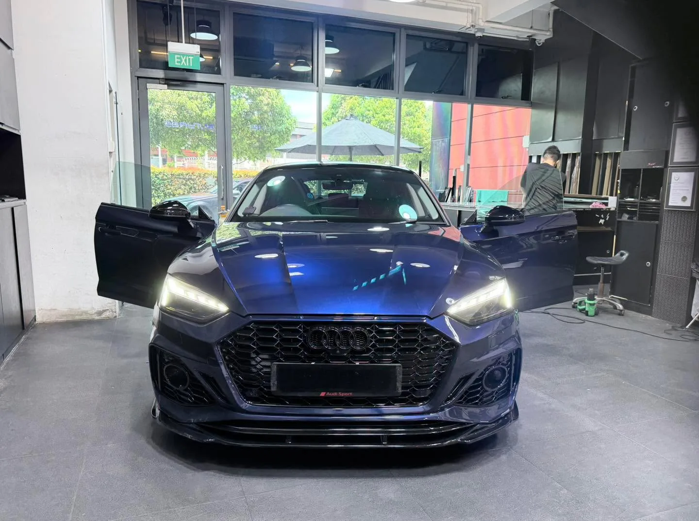 A dark blue Audi sedan with both doors open, positioned indoors at the workshop.